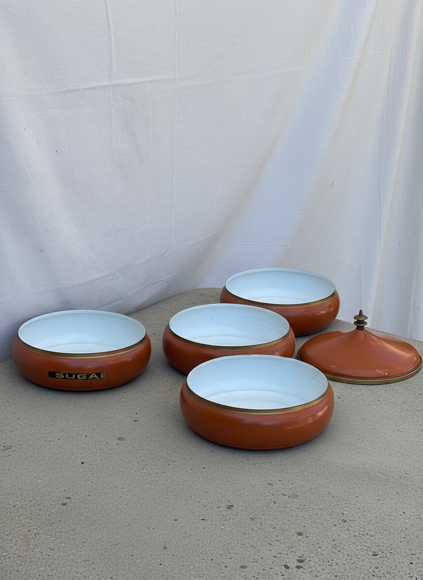 Mid-century vintage orange metal canister set from the 1960s featuring brass-tone trim and stackable design, ideal for stylish kitchen storage — Hommes and Gardens, Home Decor Collection, Decorative Jars, Vintage Decor, Retro Metal Art, Mid-Century Kitchenware, Classic Storage Jars, Decorative Home Accessories.