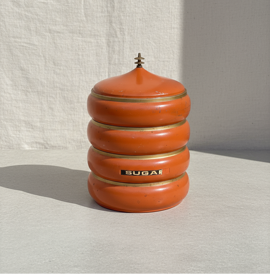 Vintage 1960s mid-century orange metal canister set with brass-tone trim and matching lids, a vibrant four-piece storage ensemble — Hommes and Gardens, Home Decor Collection, Decorative Jars, Vintage Kitchenware, Mid-Century Modern Design, Retro Storage, Metal Decor, Collectible Home Accent.