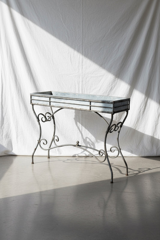 Vintage Arras style tall weathered metal plant stand, inspired by 19th-century French design, featuring elegant scrollwork and antique patina — Hommes and Gardens, Garden Collection, Plant Stands, Vintage Outdoor Decor, French Ironwork, Rustic Garden Accessories, Antique Metal Art, Botanical Display Stand.