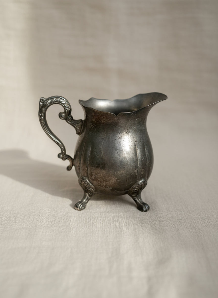 Vintage silver-plated footed creamer with curved handle and elegant reflective finish, perfect for classic tea service or collectible home display — Hommes and Gardens, Home Decor Collection, Sugar Creamers, Decorative Objects, Vintage Silverware, Antique Tableware, Elegant Dining Accent, Classic Tea Set Piece.