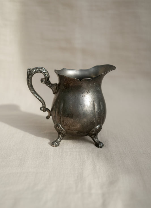 Vintage silver-plated footed creamer with curved handle and elegant reflective finish, perfect for classic tea service or collectible home display — Hommes and Gardens, Home Decor Collection, Sugar Creamers, Decorative Objects, Vintage Silverware, Antique Tableware, Elegant Dining Accent, Classic Tea Set Piece.