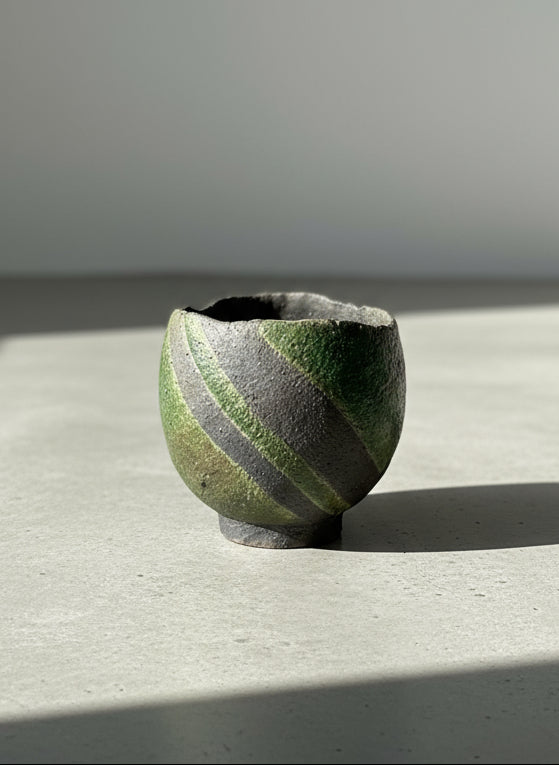 Small ceramic cup with green and black striped pattern on a textured beige background