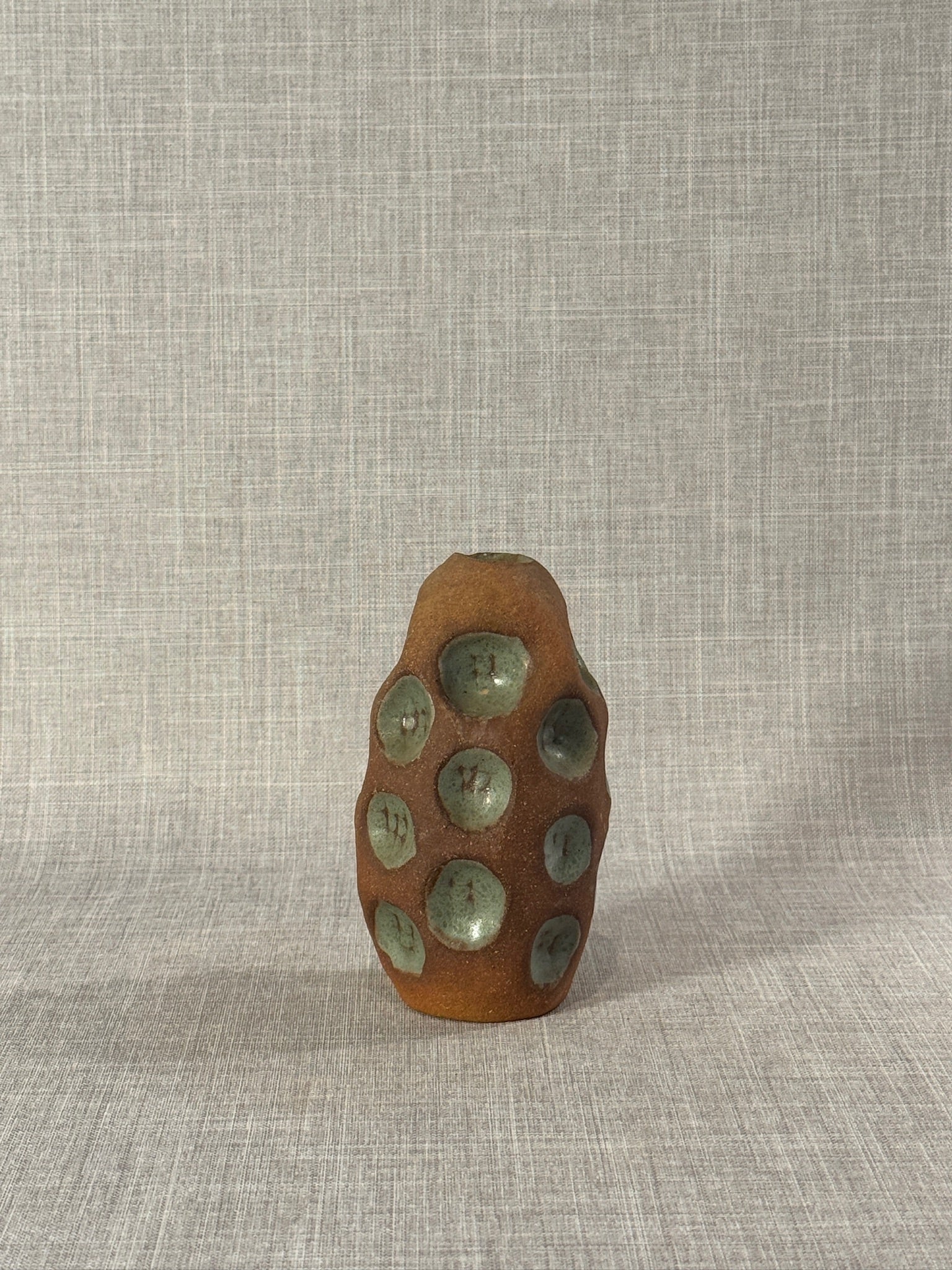 Handmade Terracotta Glazed Studio Pottery Bud Vase with Celadon Impressions on textured background, hommes + gardens estudio.