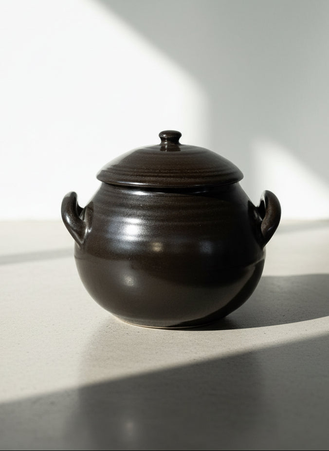Black ceramic pot with lid on a textured beige background