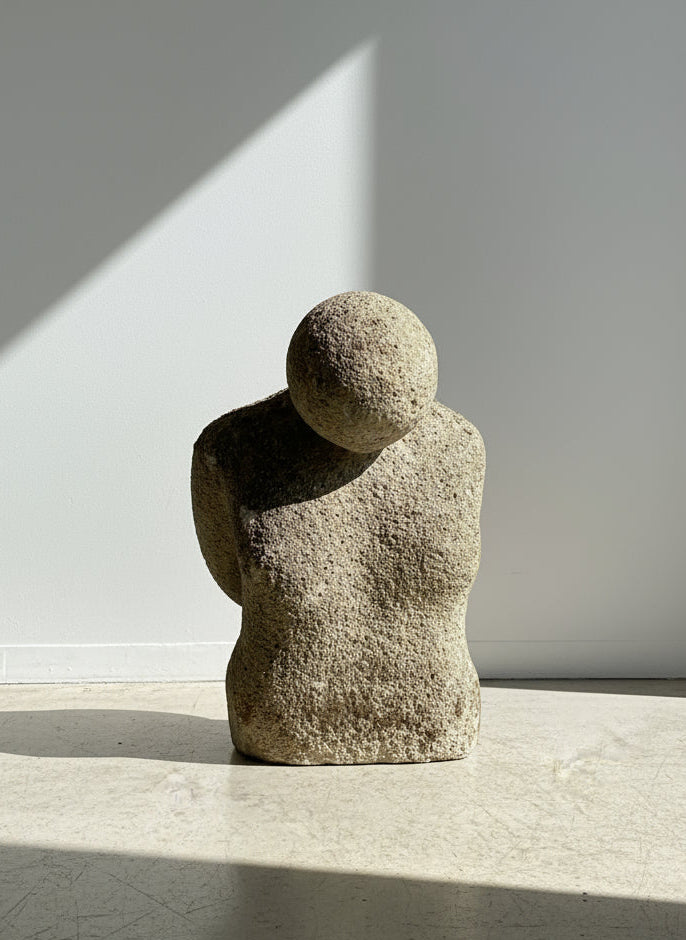 Stone sculpture of a human figure on a white pedestal against a light blue wall.