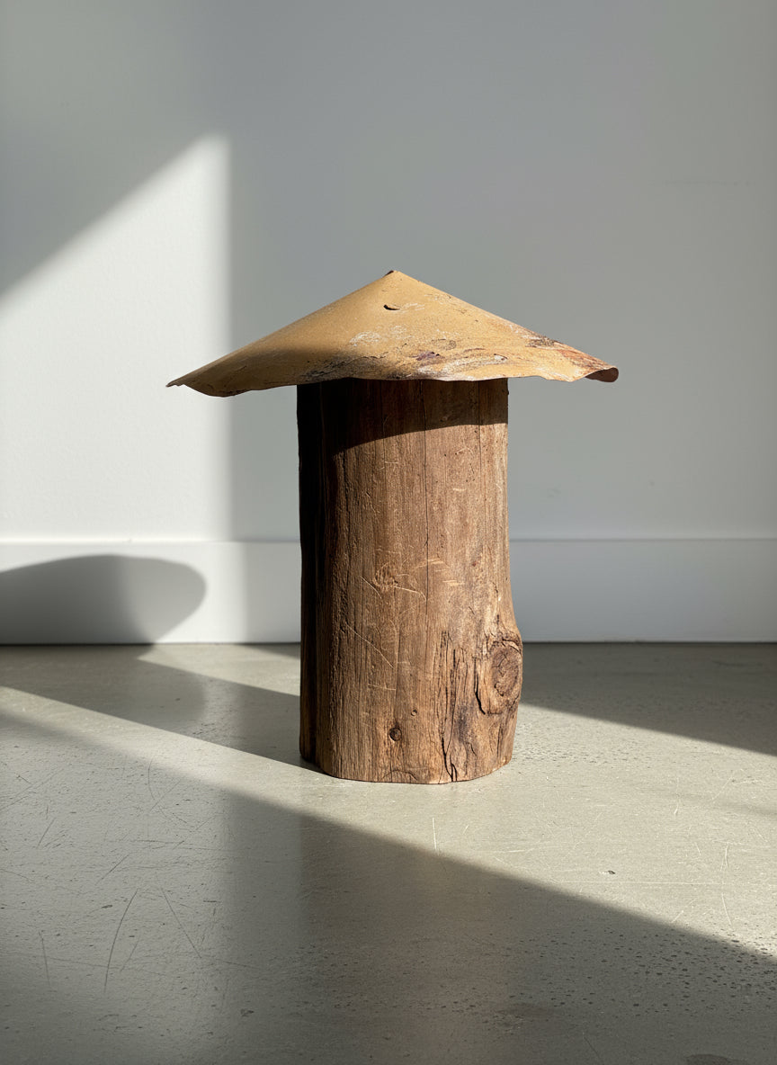 Rustic Primitive Wooden Post Sculpture with Aged Metal Roof on a concrete floor, showcasing natural textures and industrial design. hommes + gardens estudio.