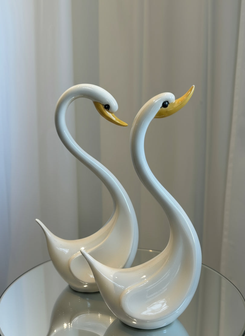 Pair of Elegant Vintage Ceramic Swan Sculptures in Gloss White with Yellow Beaks on a reflective surface, hommes + gardens estudio.