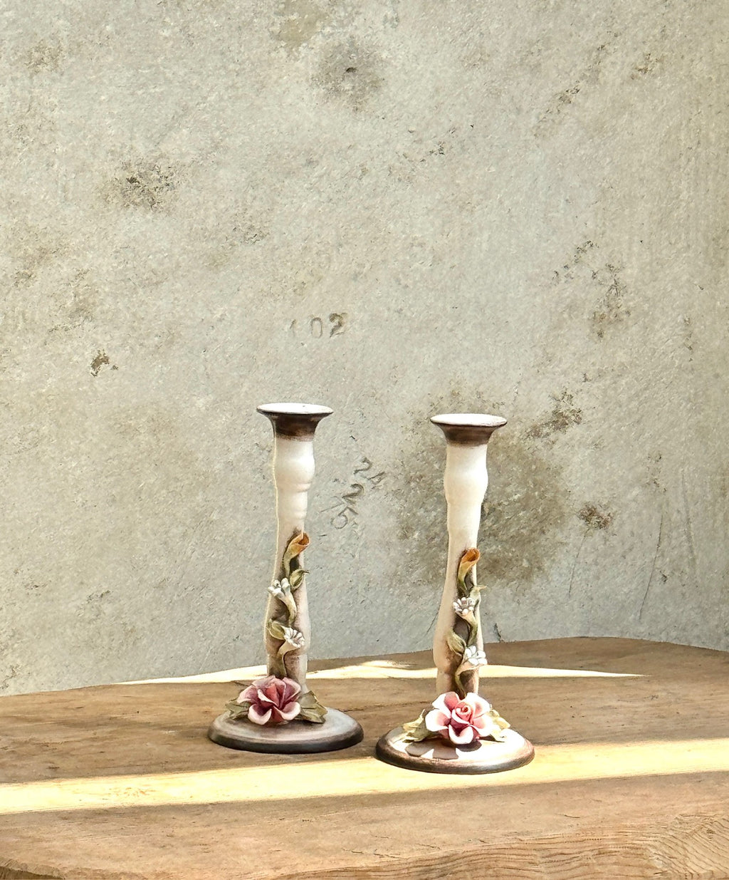 Pair of Ceramic Candlesticks with Floral Decoration on a wooden table, featuring intricate floral details. hommes + gardens estudio.