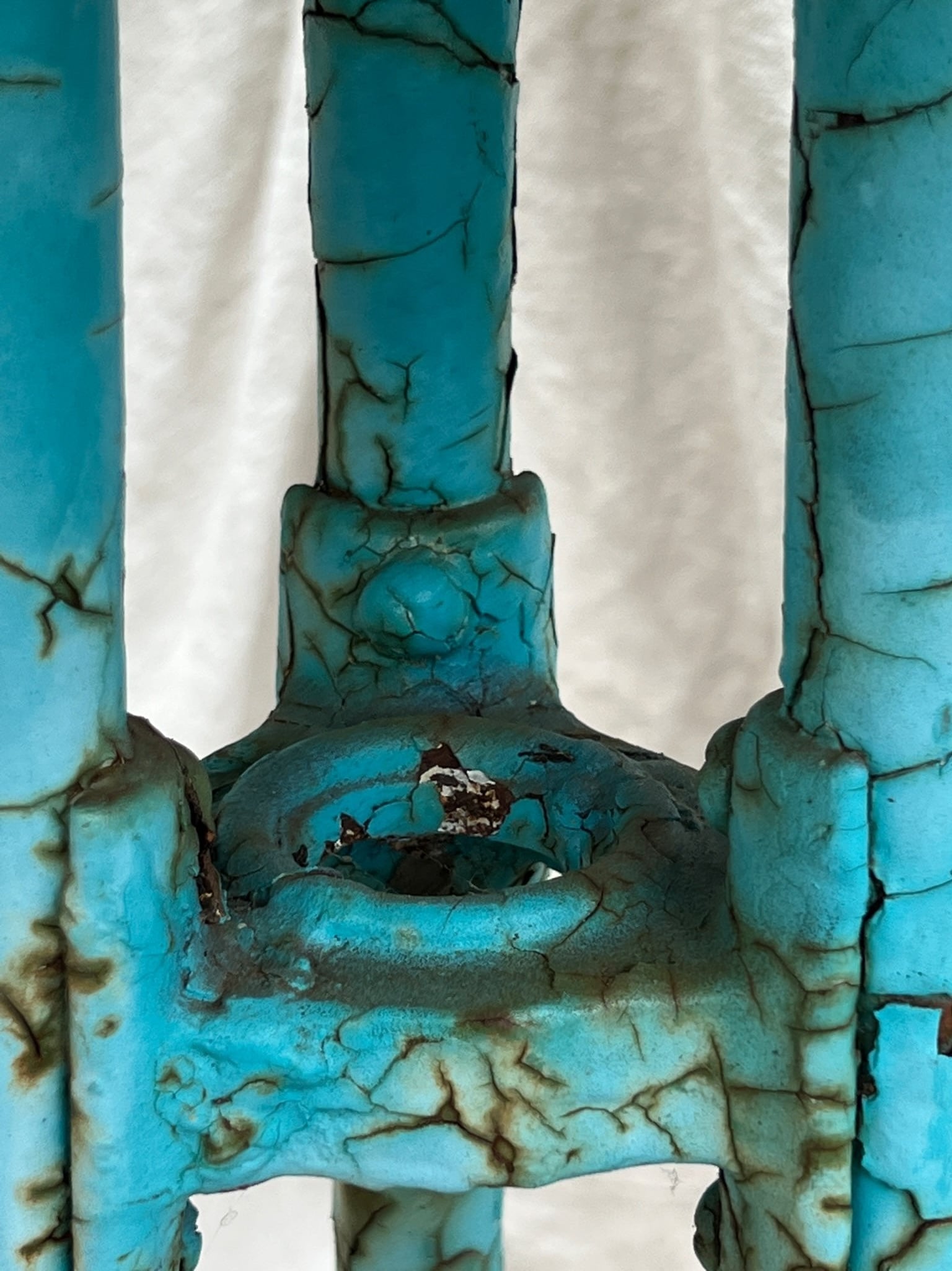 Close-up view of the base of a Vintage French Turquoise Rusted Bistro Table showcasing distressed turquoise paint. hommes + gardens estudio.