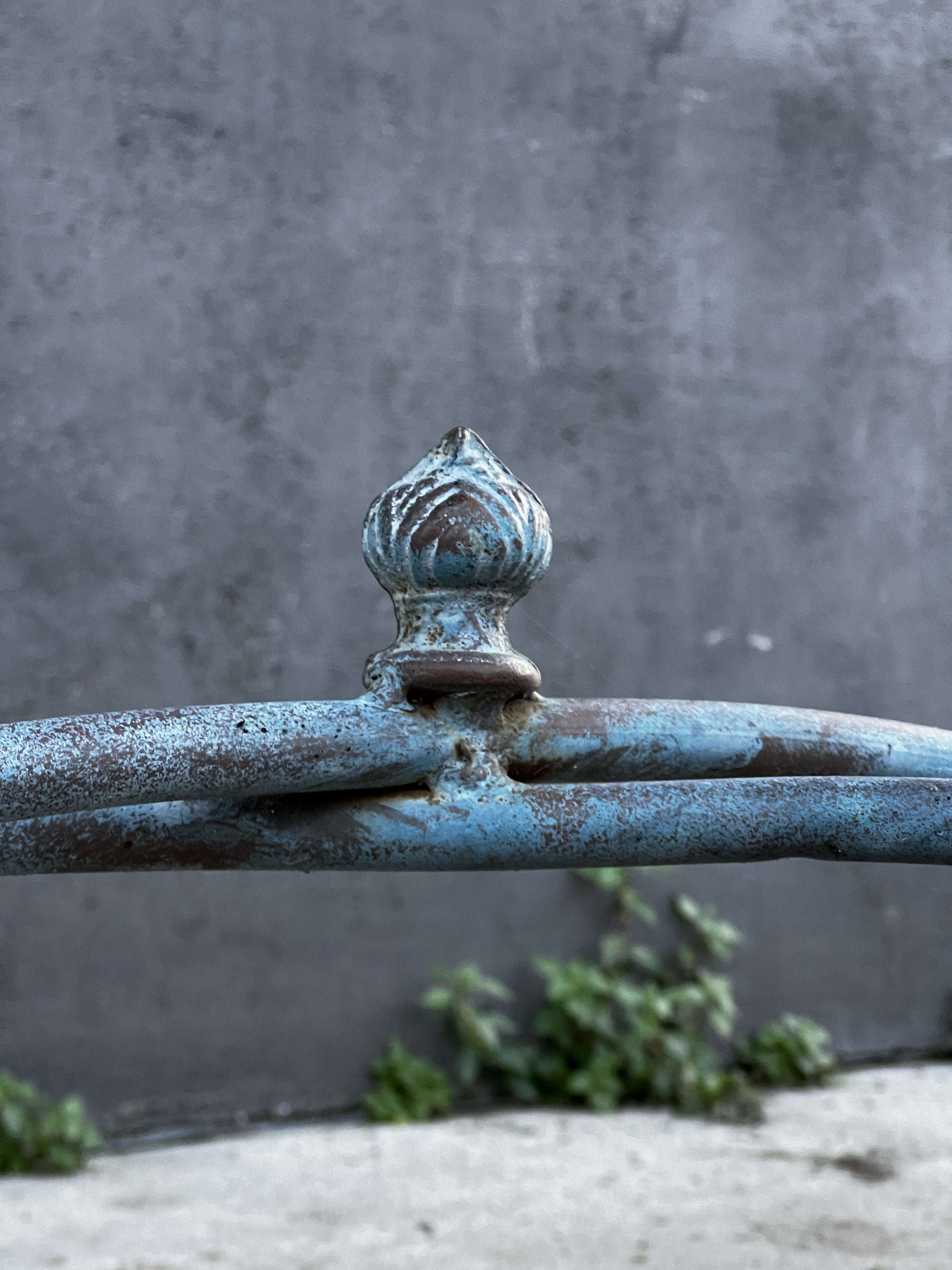 Close-up of the decorative tip of a Vintage Arras Style Tall Weathered Metal Plant Stand, showcasing its elegant details. hommes + gardens estudio.