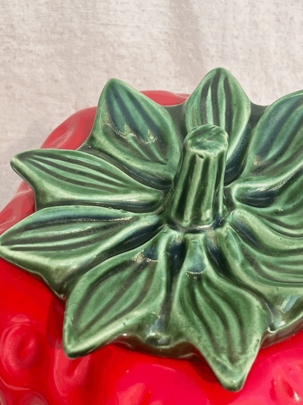 Detail of the lid of a Vintage McCoy Pottery Strawberry Cookie Jar, featuring a green leaf design on vibrant red ceramic. hommes + gardens estudio.