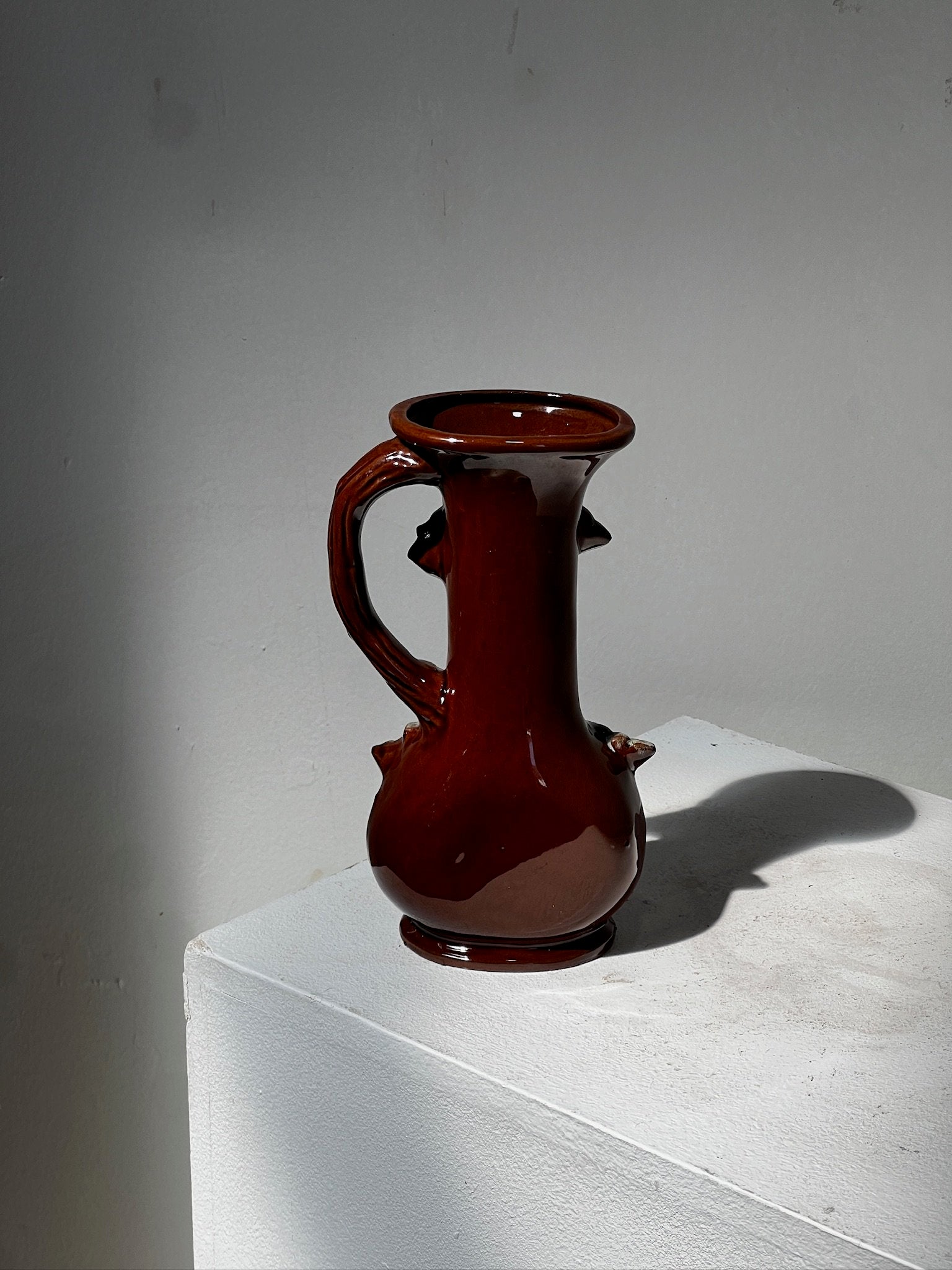 Small antique ceramic vase with 3D floral motifs displayed on a white pedestal, featuring intricate design details. hommes + gardens estudio.