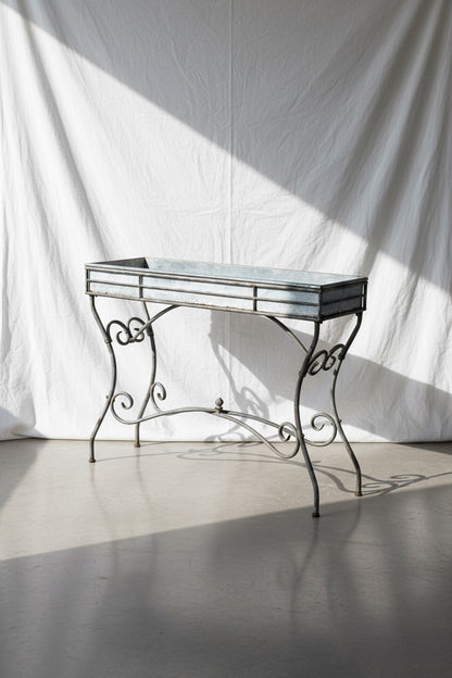 Vintage Arras style tall weathered metal plant stand, inspired by 19th-century French design, featuring elegant scrollwork and antique patina — Hommes and Gardens, Garden Collection, Plant Stands, Vintage Outdoor Decor, French Ironwork, Rustic Garden Accessories, Antique Metal Art, Botanical Display Stand.