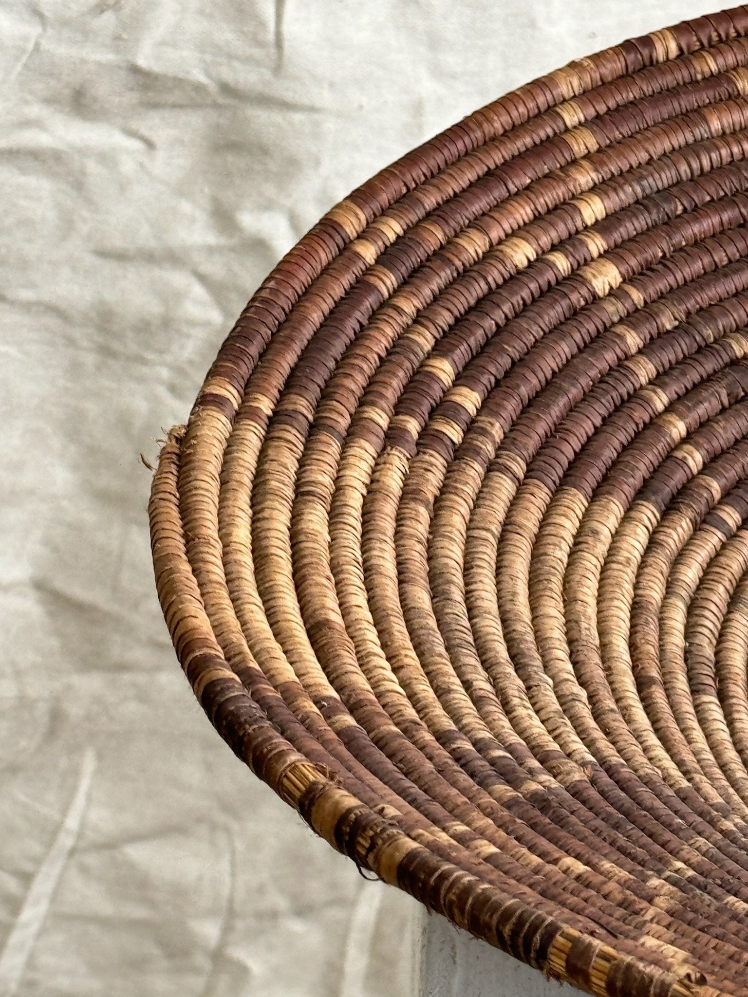 Close-up view of a Vintage Round Rattan Coiled Boho Woven Basket showcasing its intricate design and natural tones. hommes + gardens estudio.
