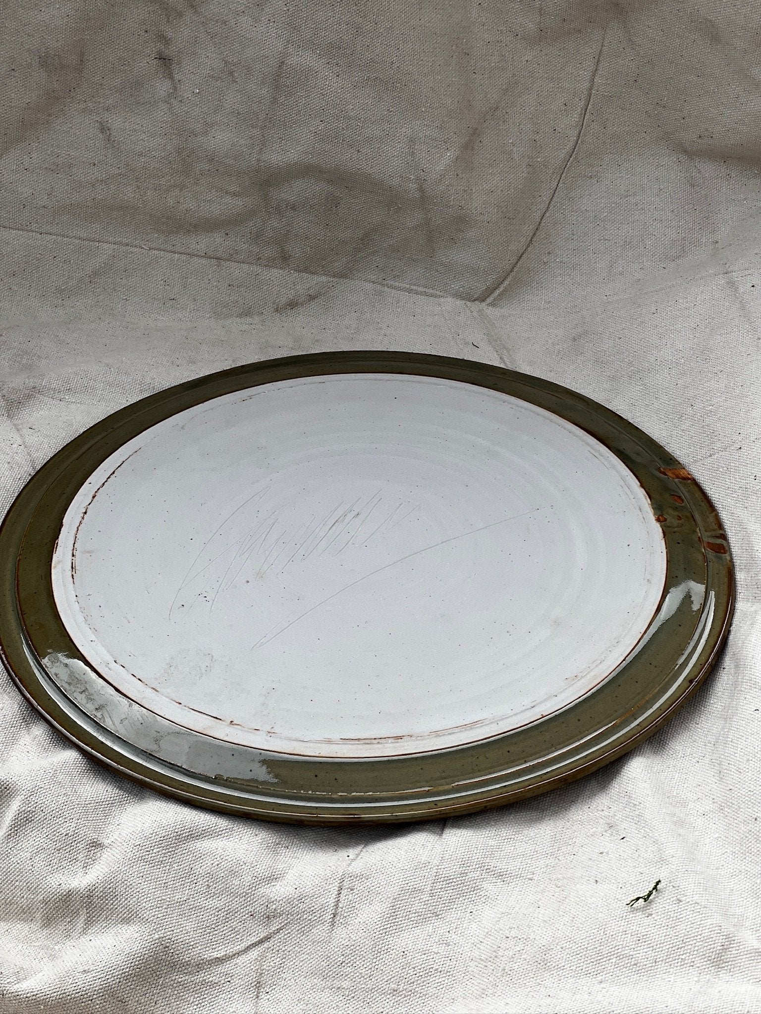 Signed vintage ceramic cake plate - earthy green displayed on a textured background, showcasing its unique design and colors. hommes + gardens estudio.