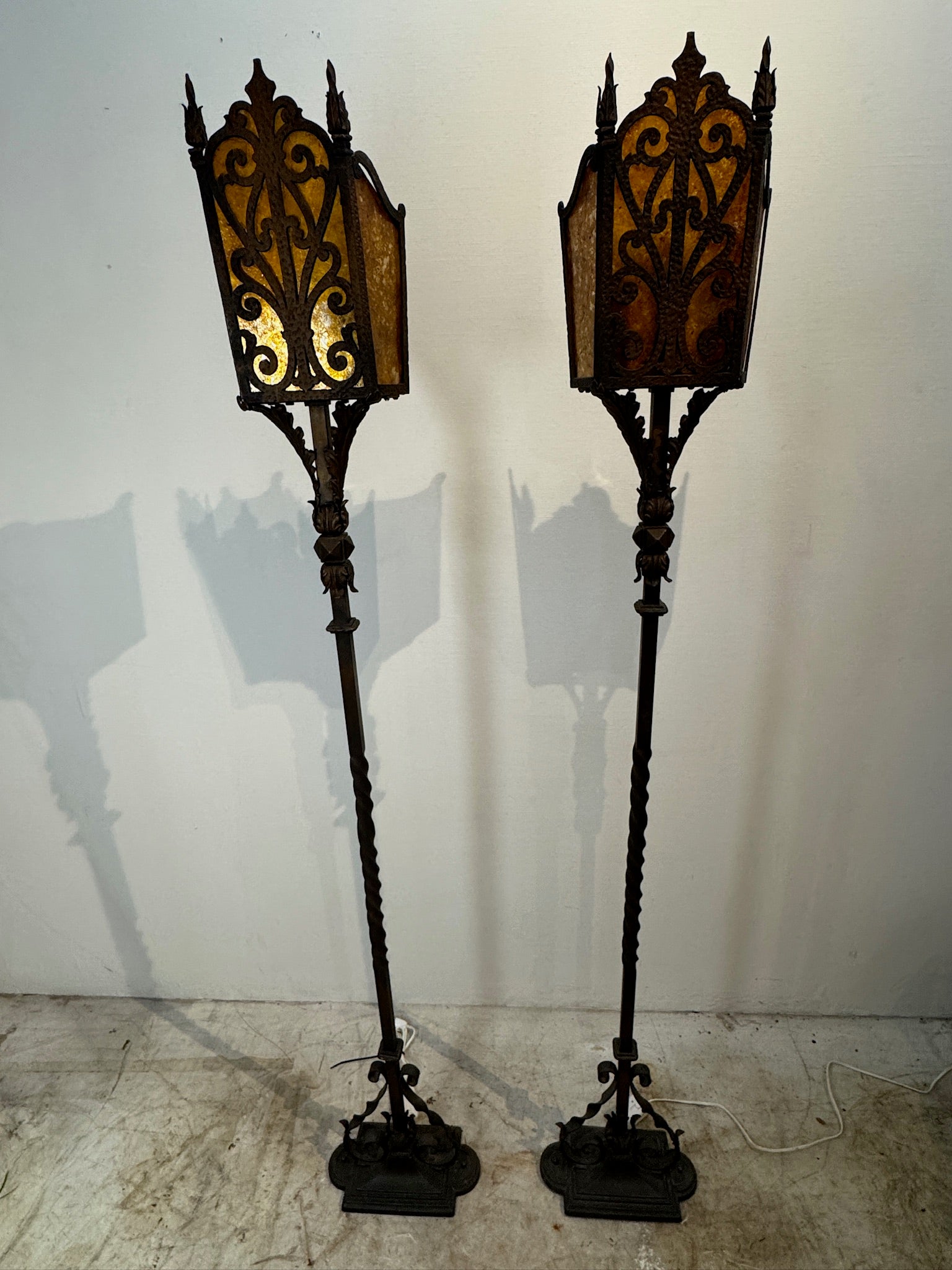 Pair of vintage wrought iron floor lamps with amber mica shades in Mission style, featuring scrollwork bases and warm glowing light — Hommes and Gardens, Lights + Lanterns Collection, Landscape Architect, Interior Designer, Outdoor Living, Art, Furniture, Objects, Best Gifts, Nature, Backyard, Yard, Outdoor Decorations, Home Decor, Home Design, Luxury Design.