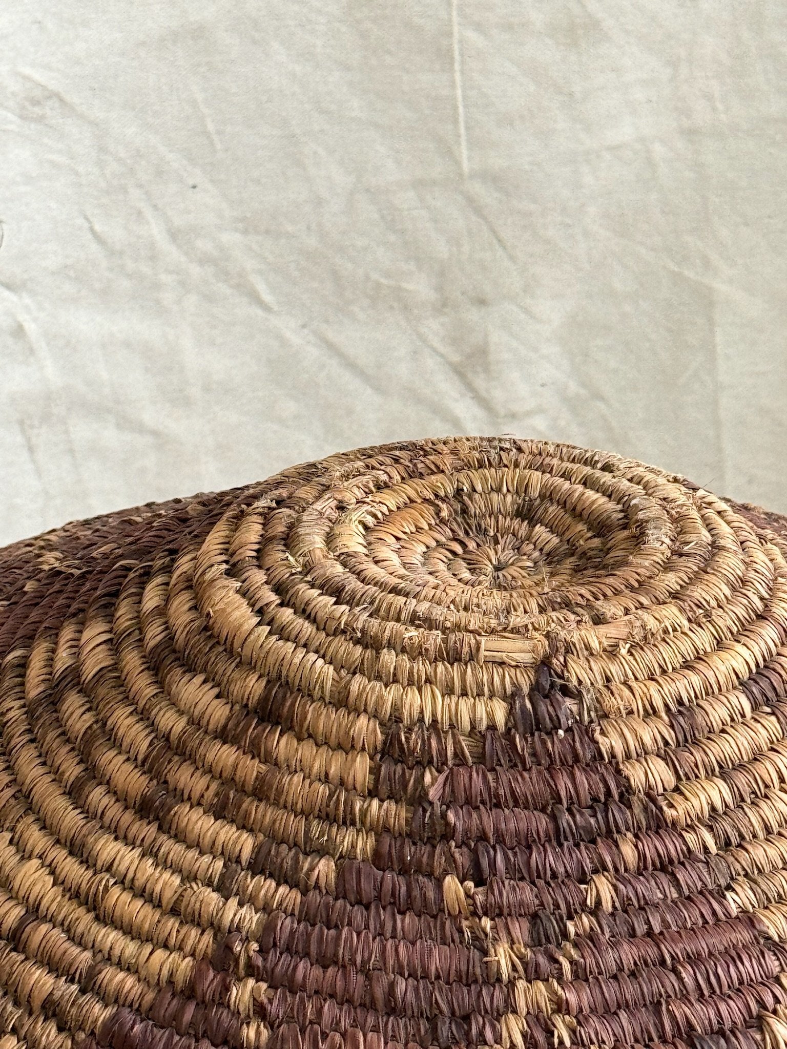 Top view of a Vintage Round Rattan Coiled Boho Woven Basket showcasing its intricate weaving and natural colors. hommes + gardens estudio.