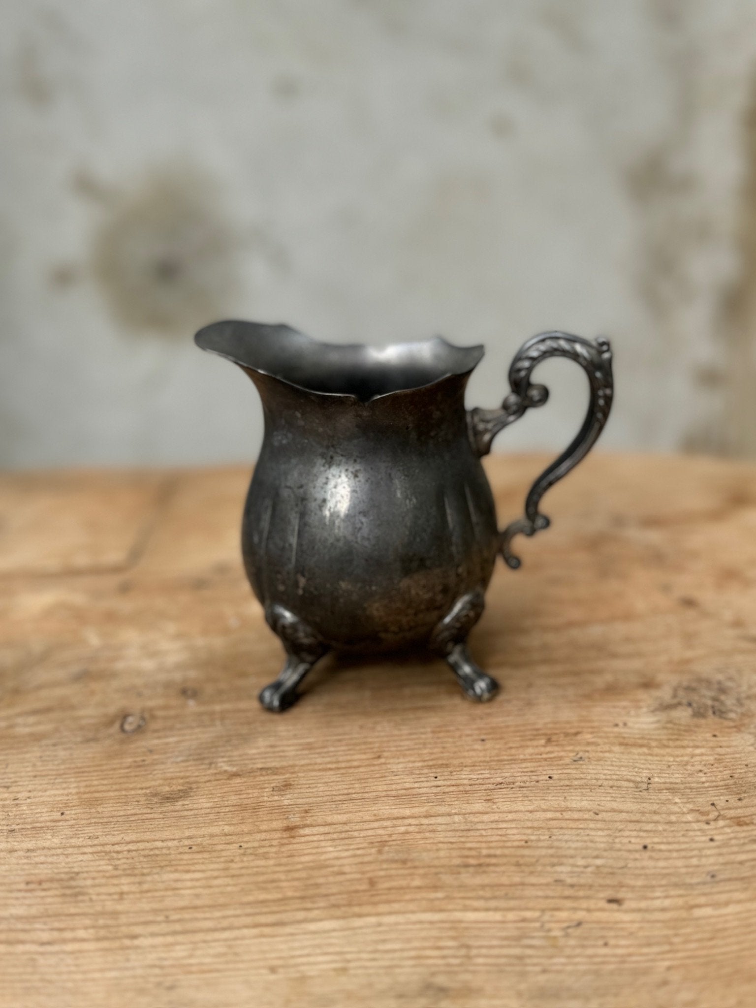Vintage Silver-Plated Footed Creamer with Handle on wooden table, showcasing its elegant design and vintage charm. hommes + gardens estudio.