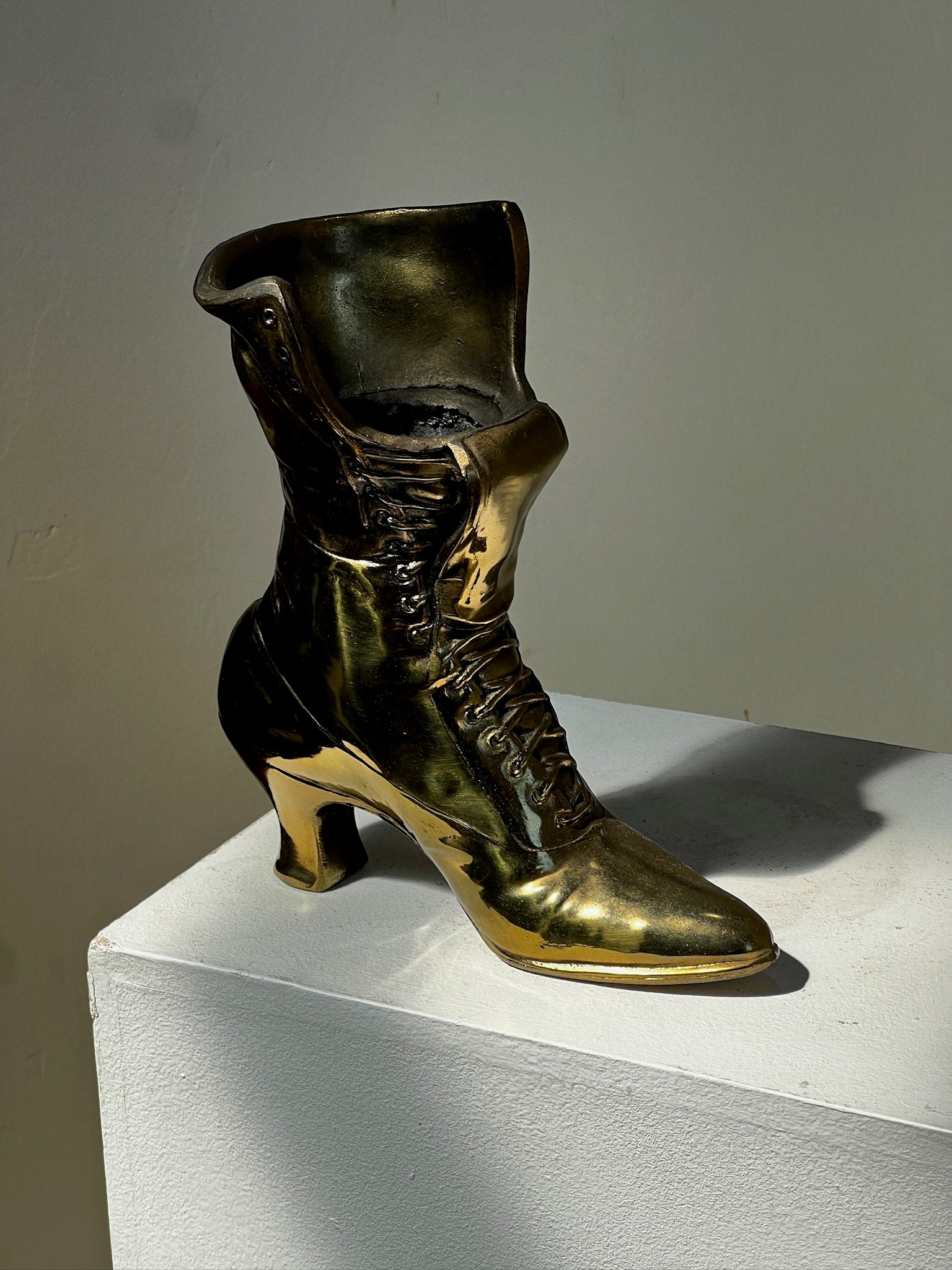 Vintage Victoria style cast brass boot window planter displayed on a pedestal, showcasing intricate details and elegance. hommes + gardens estudio.