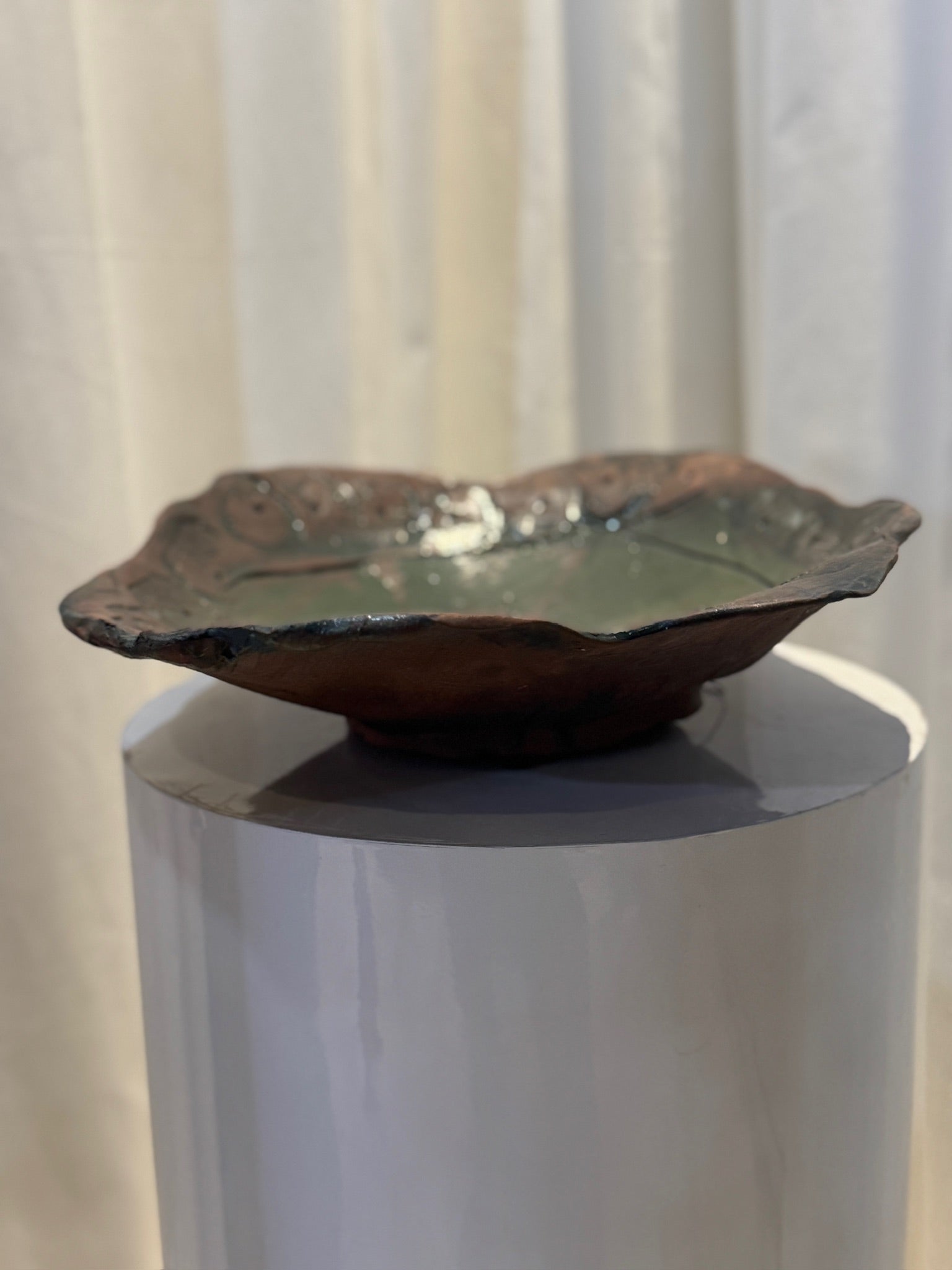 Unique Handcrafted Ceramic Art Bowl with Green Glaze and Sculptural Organic Edge displayed on a pedestal. hommes + gardens estudio.